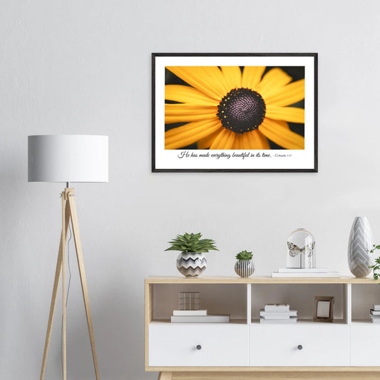 A framed art print of a close-up yellow flower with a quote from Ecclesiastes 3:11, 'He has made everything beautiful in its time.' displayed in a bright minimalist room with a small decors.