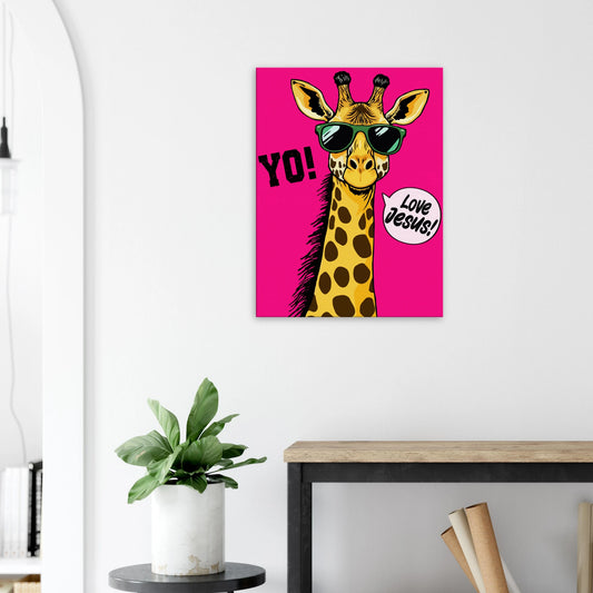 A vibrant pink poster featuring a cartoon giraffe with sunglasses and a speech bubble with the phrase 'Love Jesus!' The giraffe is the central figure against a vivid pink background displayed in a bright minimalist room with small plant decor