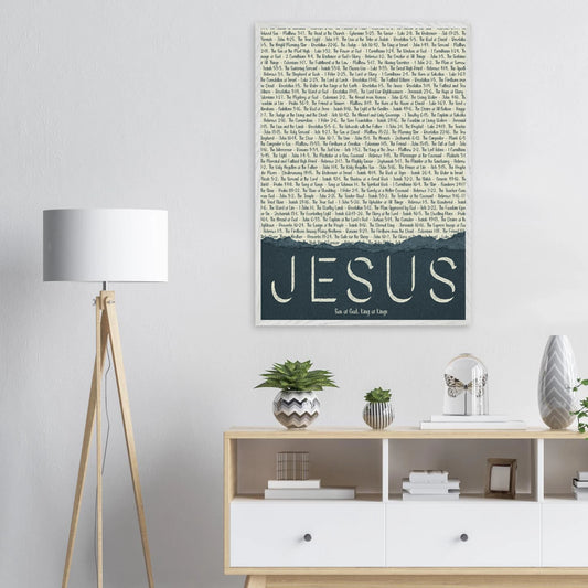 A framed wall art print with the word 'JESUS' in bold lettering, followed by a list of names and scriptures related to Jesus, against a white background displayed in a bright minimalist room with lamp and plants decor