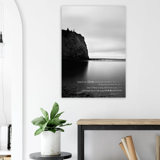 Canvas print with a black and white landscape of a cliff over water, mounted on a wall above a desk.