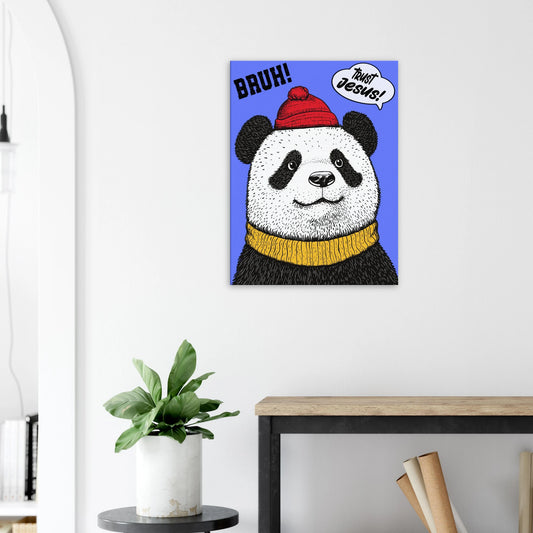 A canvas wall art featuring a cartoon illustration of a panda with a red beanie hat, a yellow scarf, and a speech bubble saying 'Trust Jesus' with a blue background displayed in a bright minimalist room with a small plant decor.
