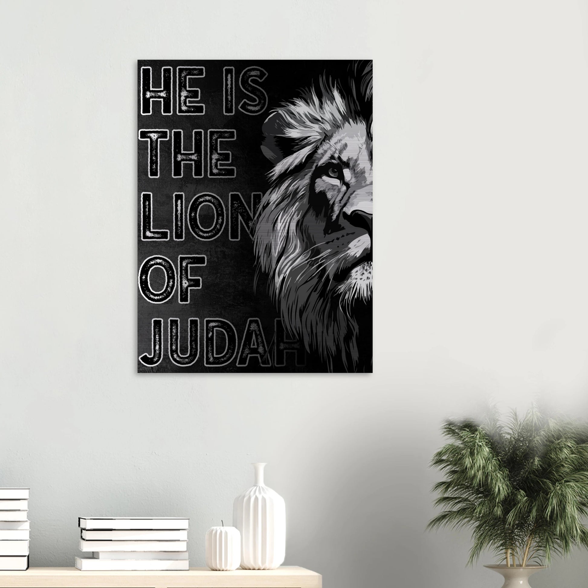 Christian wall art print featuring a black and white illustration of a lion with the text HE IS THE LION OF JUDAH, displayed above a wooden console with books and a white vase.