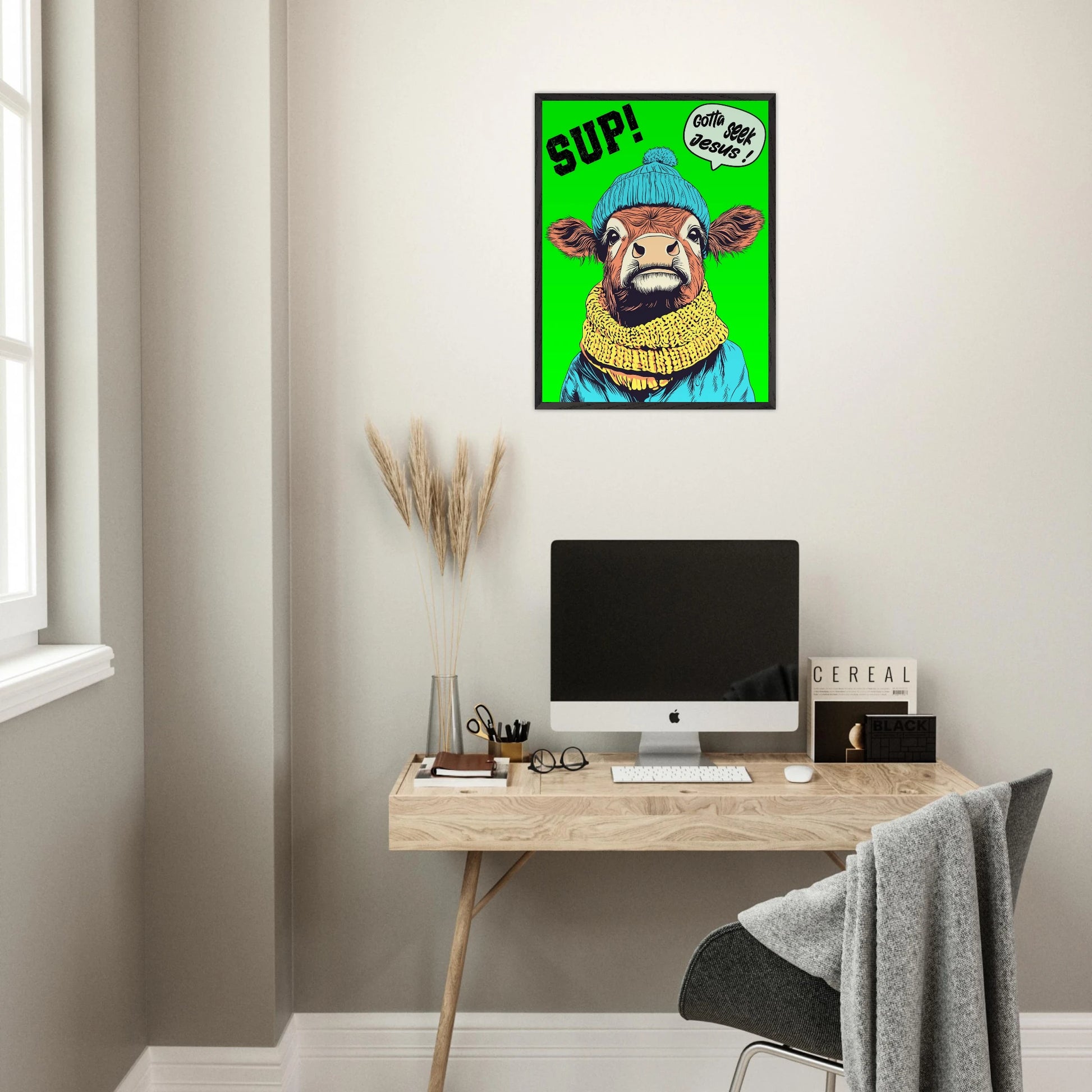 Playful Christian wall art featuring an illustrated cow wearing a blue beanie and yellow scarf on a bright green background, with SUP! and Gotta seek Jesus in a speech bubble, framed and displayed above a modern home office desk setup
