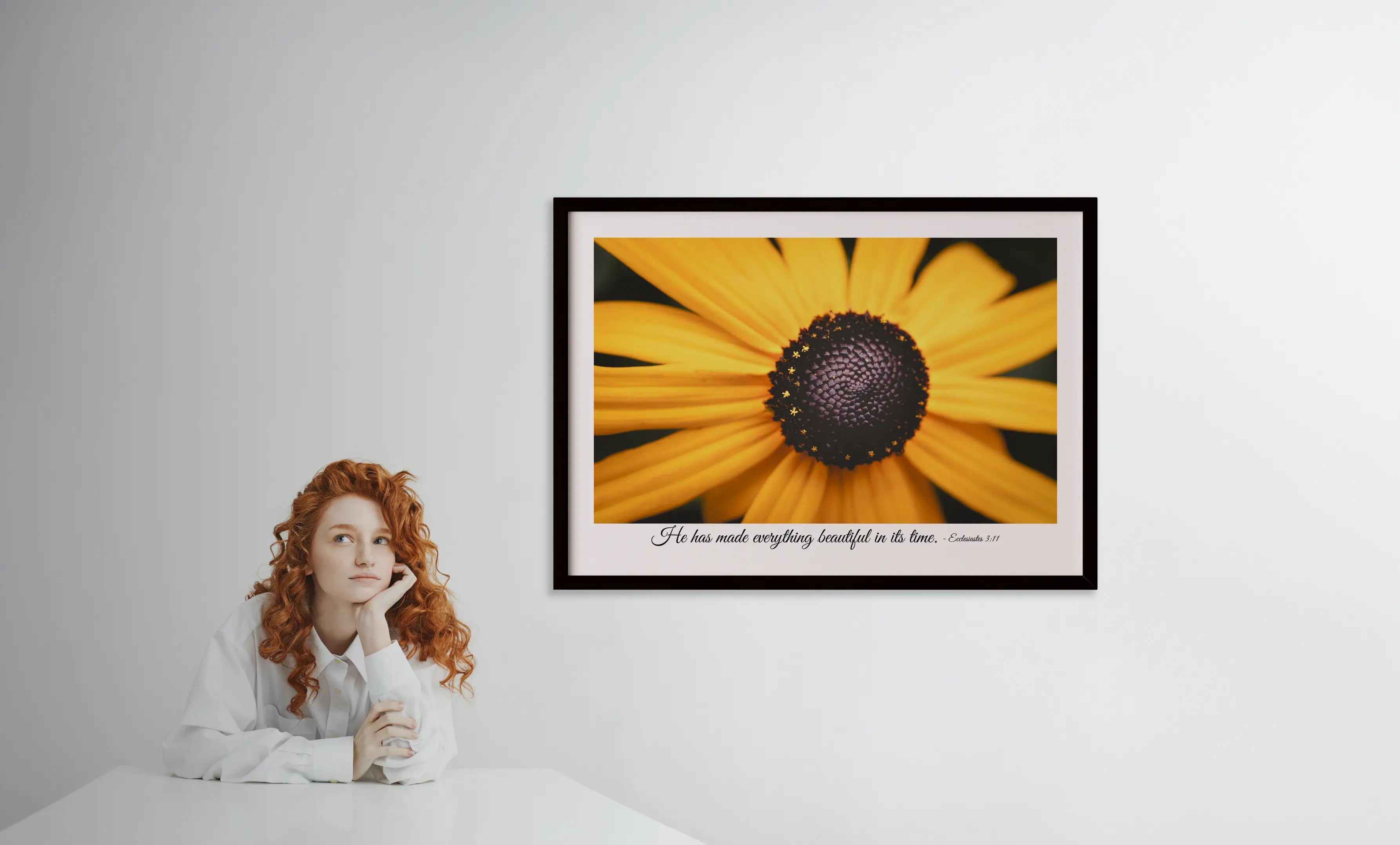 Framed photograph of a sunflower with a quote on a white wall, person sitting in front.
