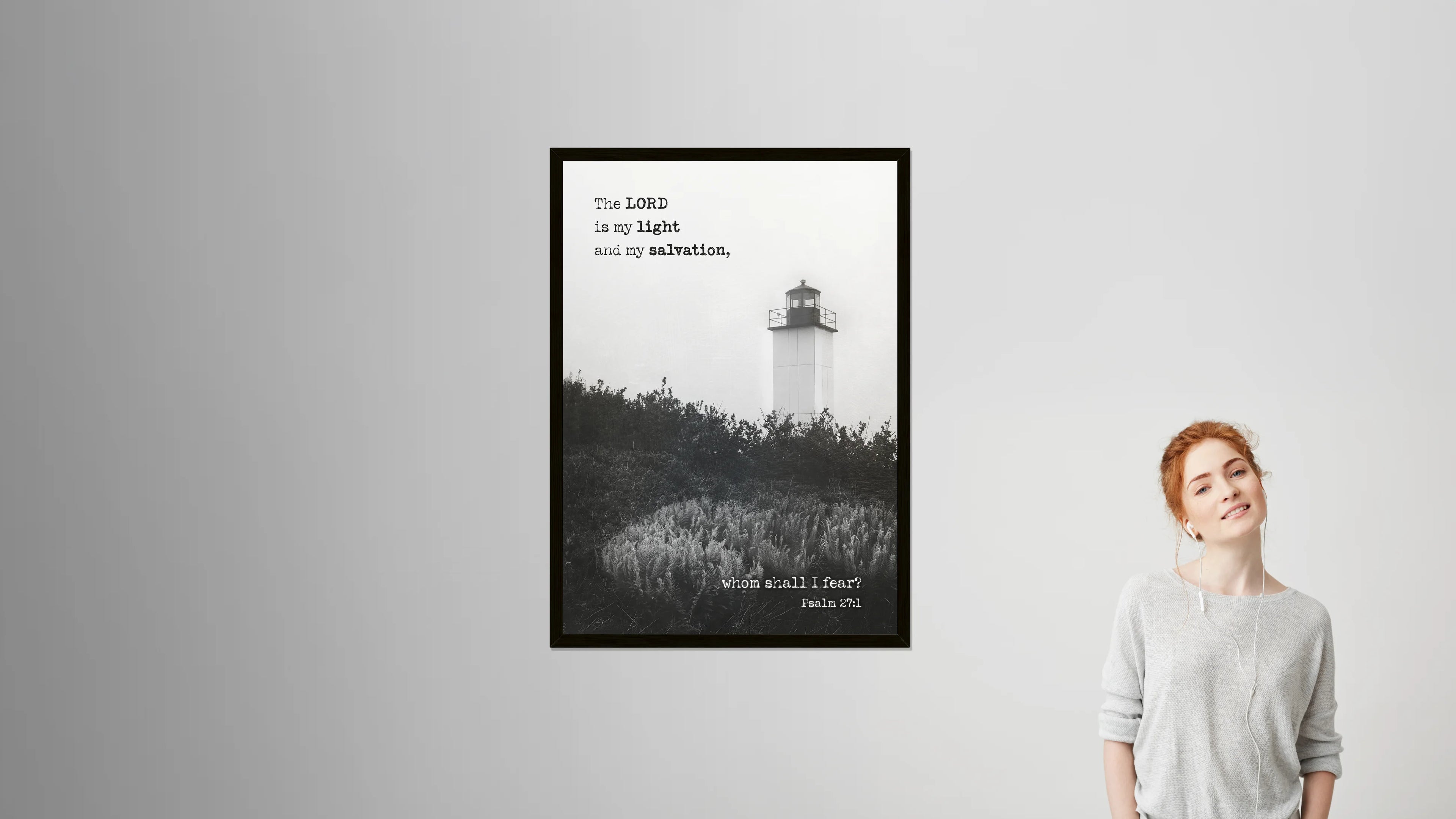 Framed poster of a lighthouse with a quote on a gray wall, next to a person.