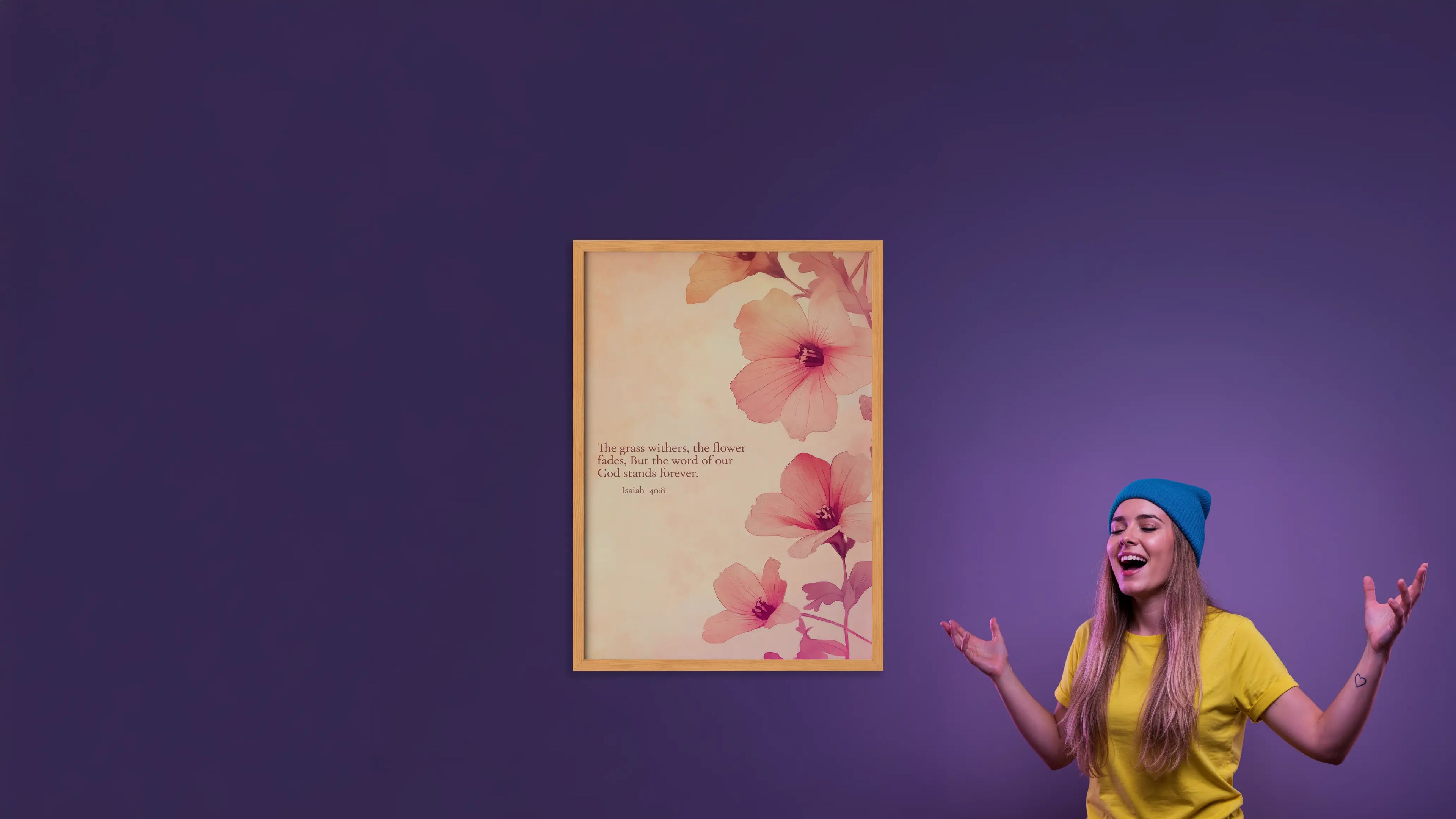 Woman in yellow shirt and blue beanie standing next to a floral framed picture on a purple wall