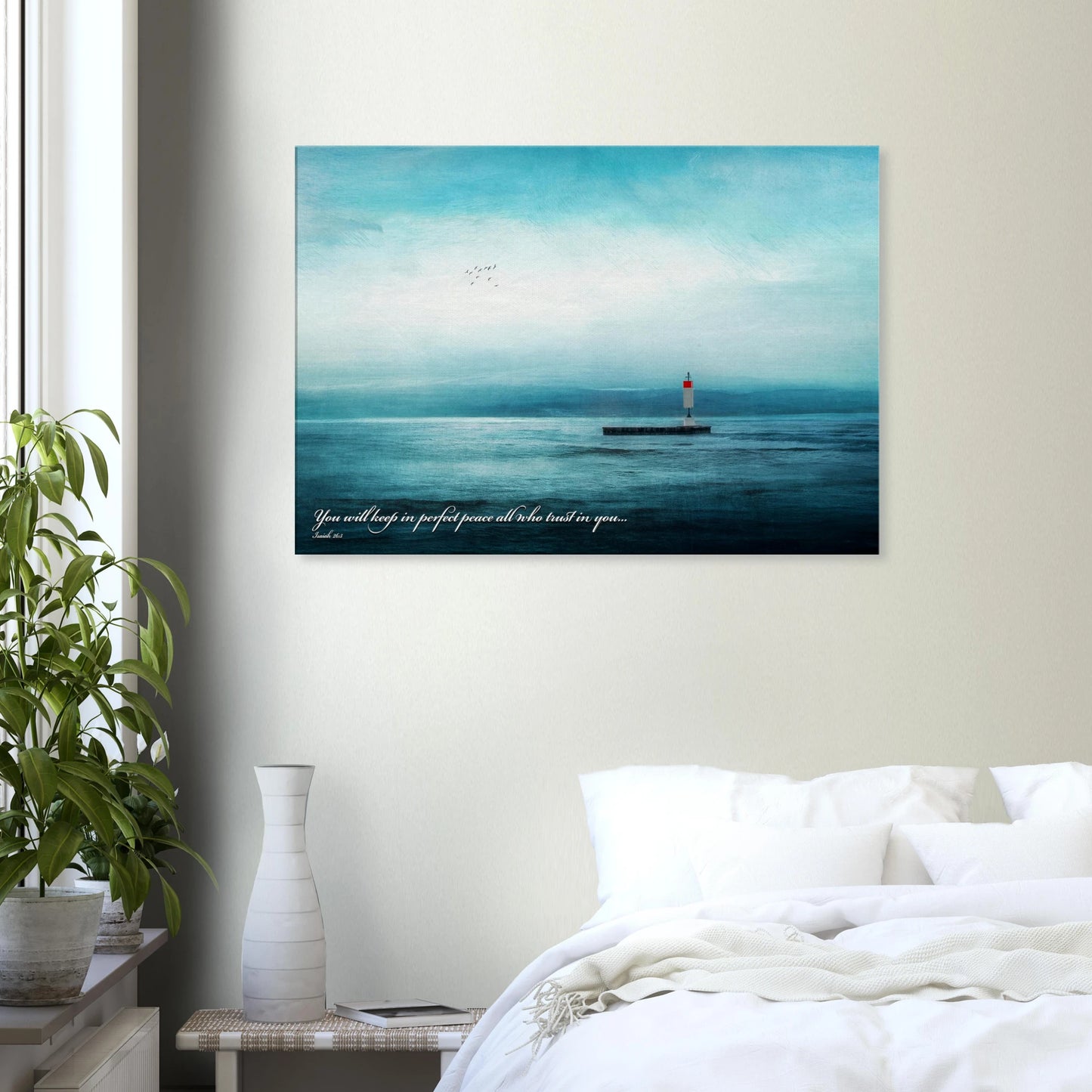 A wall art print featuring a lighthouse with a backdrop of the sea and sky, including a quote about perfect peace displayed in a bright minimalist bedroom with plant decor
