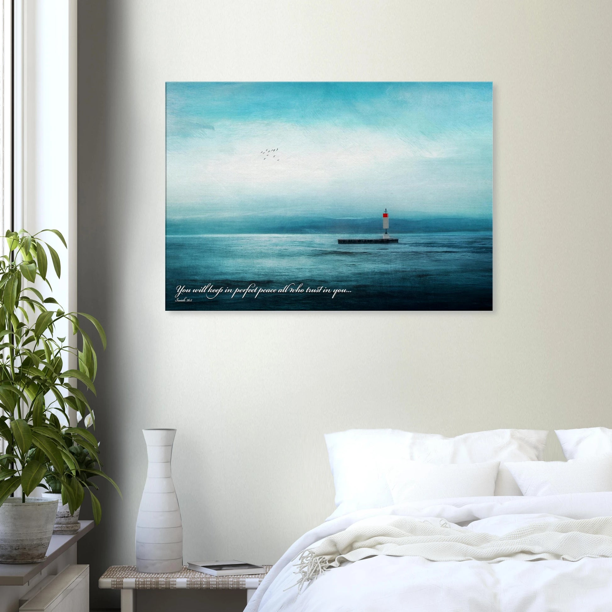 A wall art print featuring a lighthouse with a backdrop of the sea and sky, including a quote about perfect peace displayed in a bright minimalist bedroom with plant decor