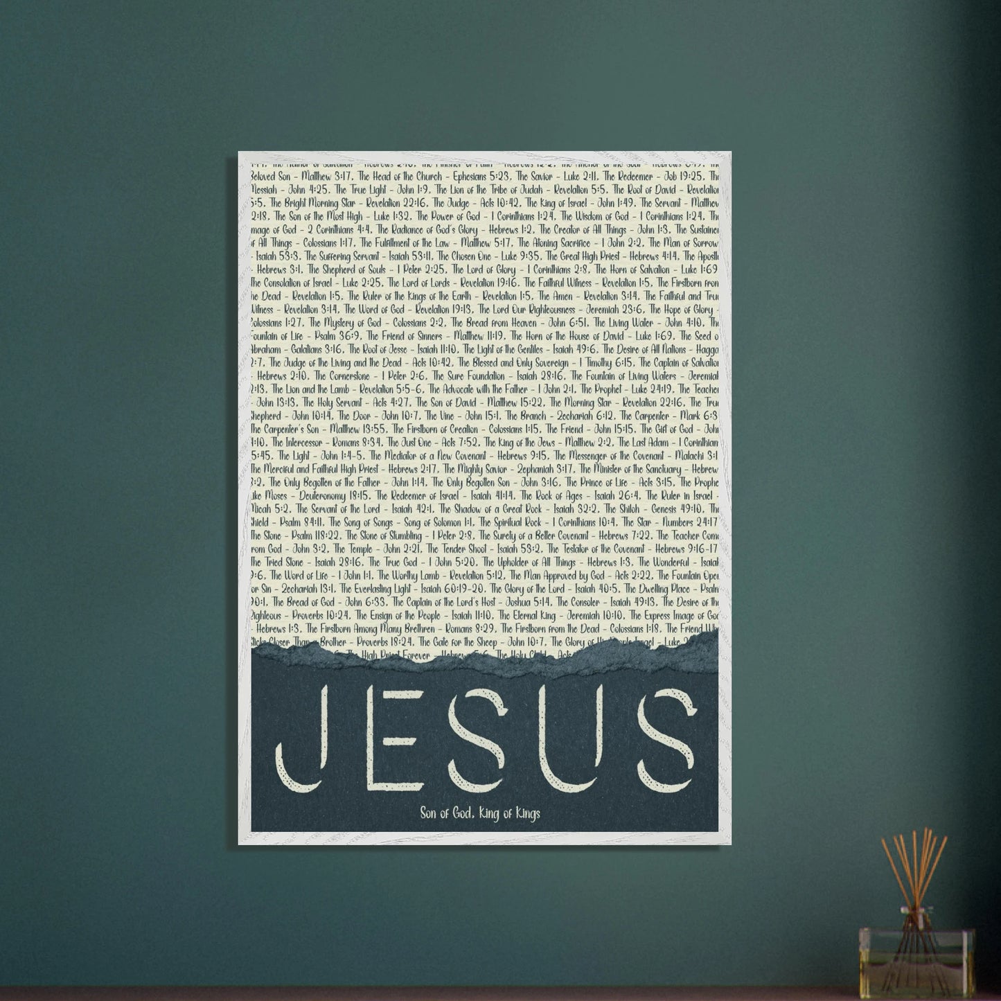 A framed wall art print with the word 'JESUS' in bold lettering, followed by a list of names and scriptures related to Jesus, against a white background hanging on a green wall with oil scent decor
