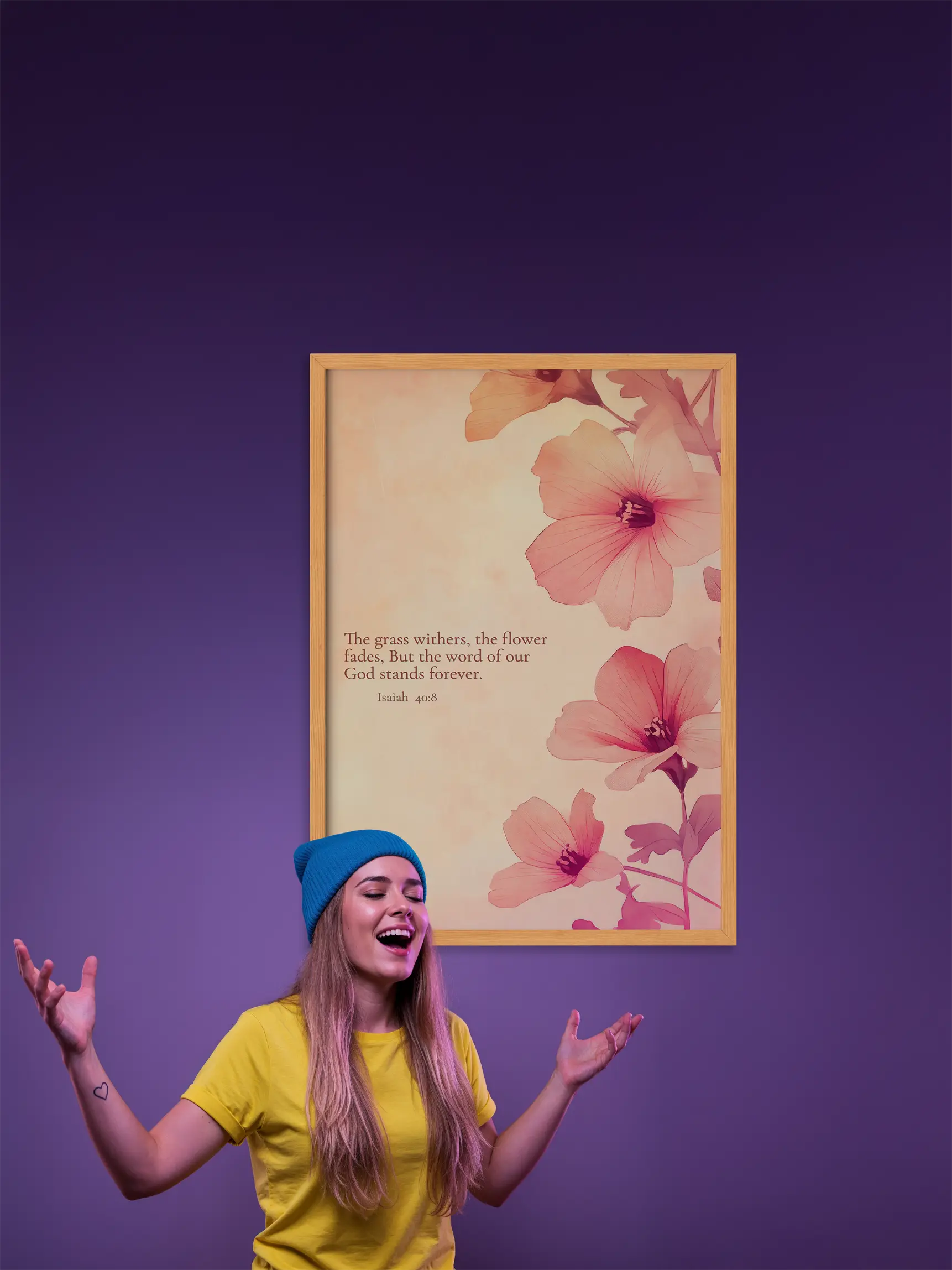 Woman in yellow shirt and blue beanie standing next to a floral framed poster on a purple background