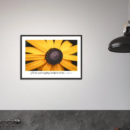 A framed art print of a close-up yellow flower with a quote from Ecclesiastes 3:11, 'He has made everything beautiful in its time.' displayed in a bright minimalist black and white kitchen