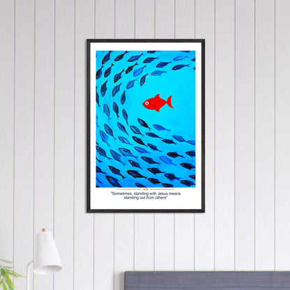Framed Christian wall art featuring a red fish swimming in water with blue fish, and the text 'Sometimes standing with Jesus means standing out from others' as a quote displayed in a bright modern minimalist room