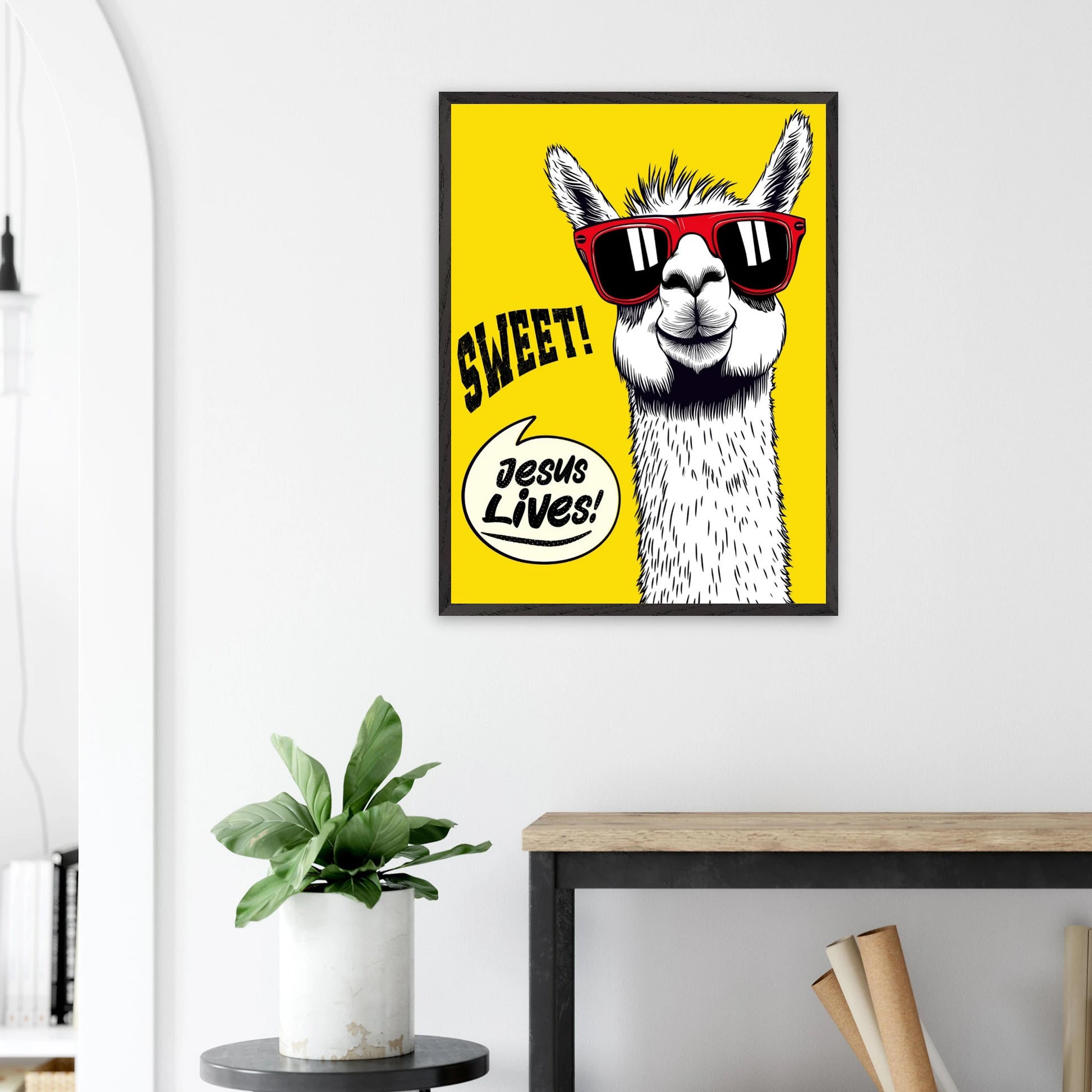Framed Christian wall art featuring a white llama wearing red sunglasses on a bright yellow background with playful text reading SWEET and Jesus Lives, displayed above a plant on a side table in a bright modern living room