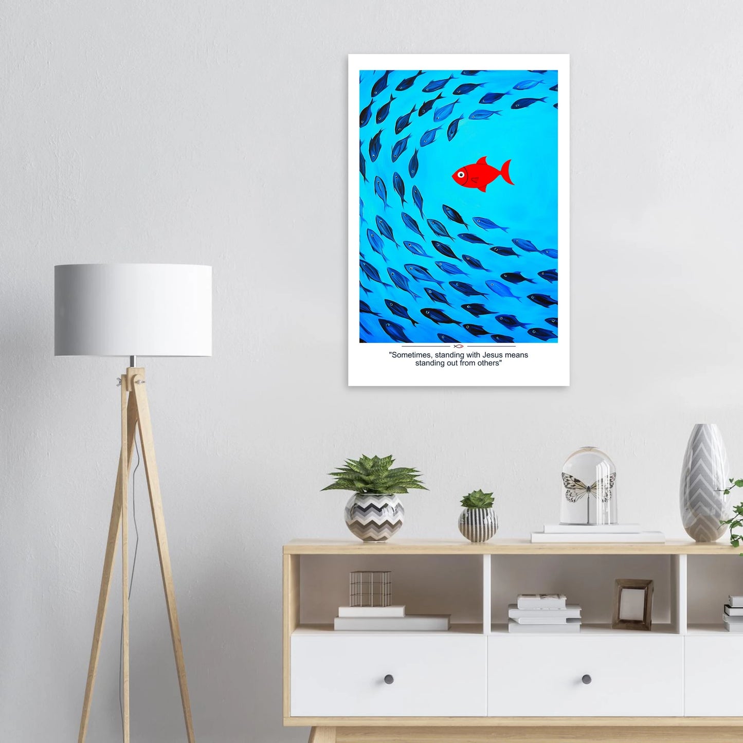 Christian wall art showing a red fish swimming against a school of blue fish with the message Sometimes standing with Jesus means standing out displayed in a bright modern minimalist room