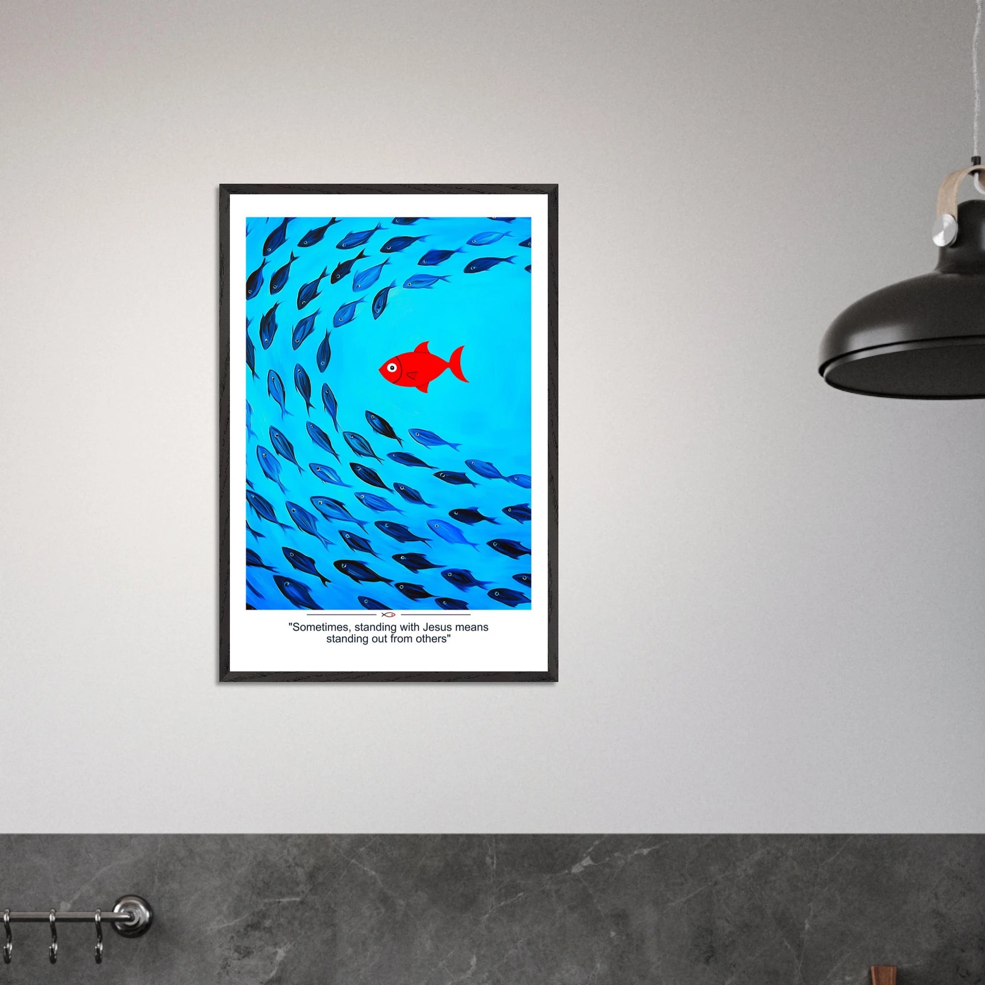 Framed Christian wall art featuring a red fish swimming in water with blue fish, and the text 'Sometimes standing with Jesus means standing out from others' as a quote displayed in a  modern minimalist room