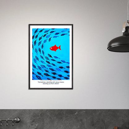 Framed Christian wall art featuring a red fish swimming in water with blue fish, and the text 'Sometimes standing with Jesus means standing out from others' as a quote displayed in a  modern minimalist room