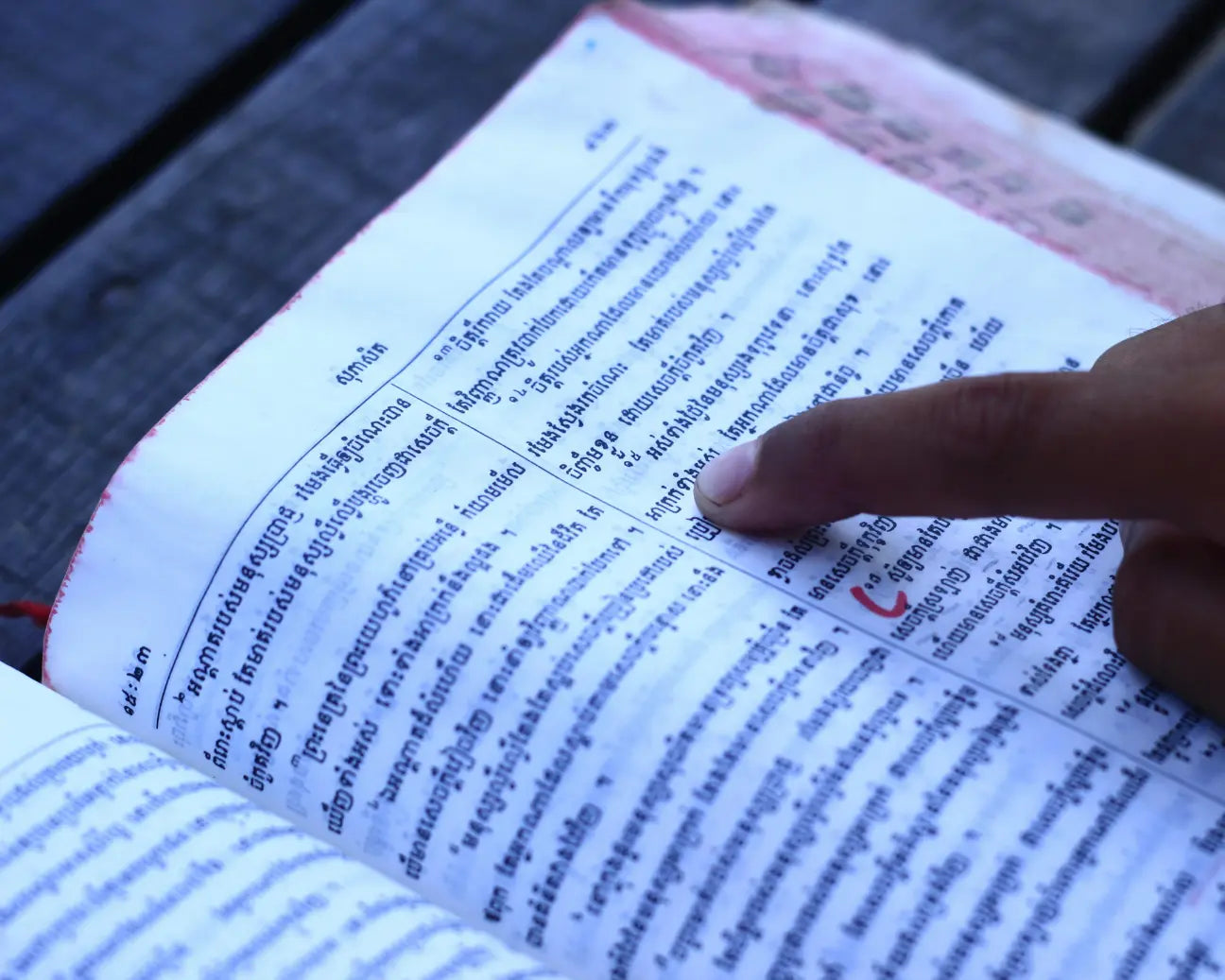 Hand pointing to text in an open book on a wooden surface
