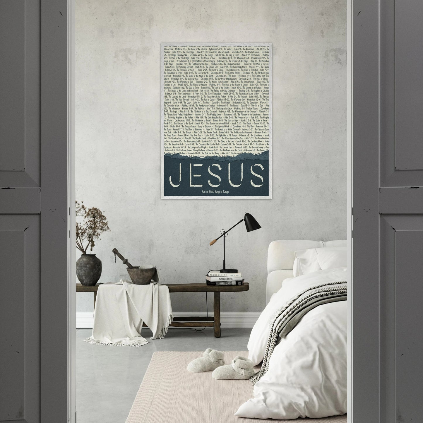A framed wall art print with the word 'JESUS' in bold lettering, followed by a list of names and scriptures related to Jesus, against a white background displayed in a bright bedroom