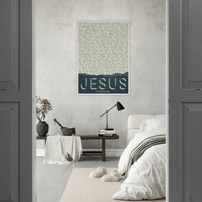 A framed wall art print with the word 'JESUS' in bold lettering, followed by a list of names and scriptures related to Jesus, against a white background displayed in a bright bedroom