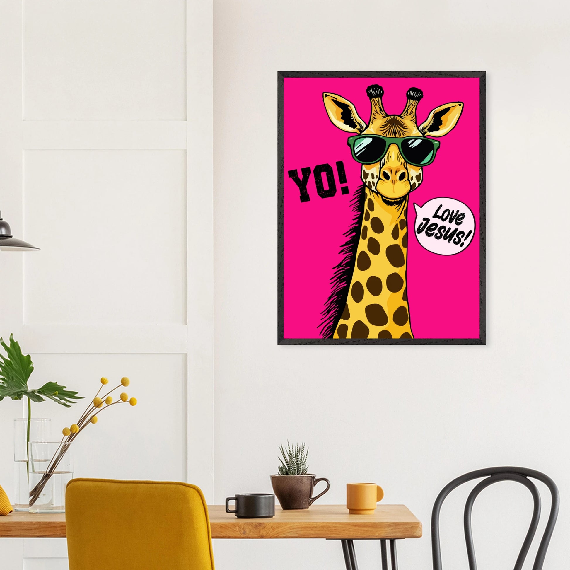 Playful Christian wall art showing a giraffe wearing sunglasses on a bright pink background with the words Yo and Love Jesus hanging above a wooden table in a modern dining space