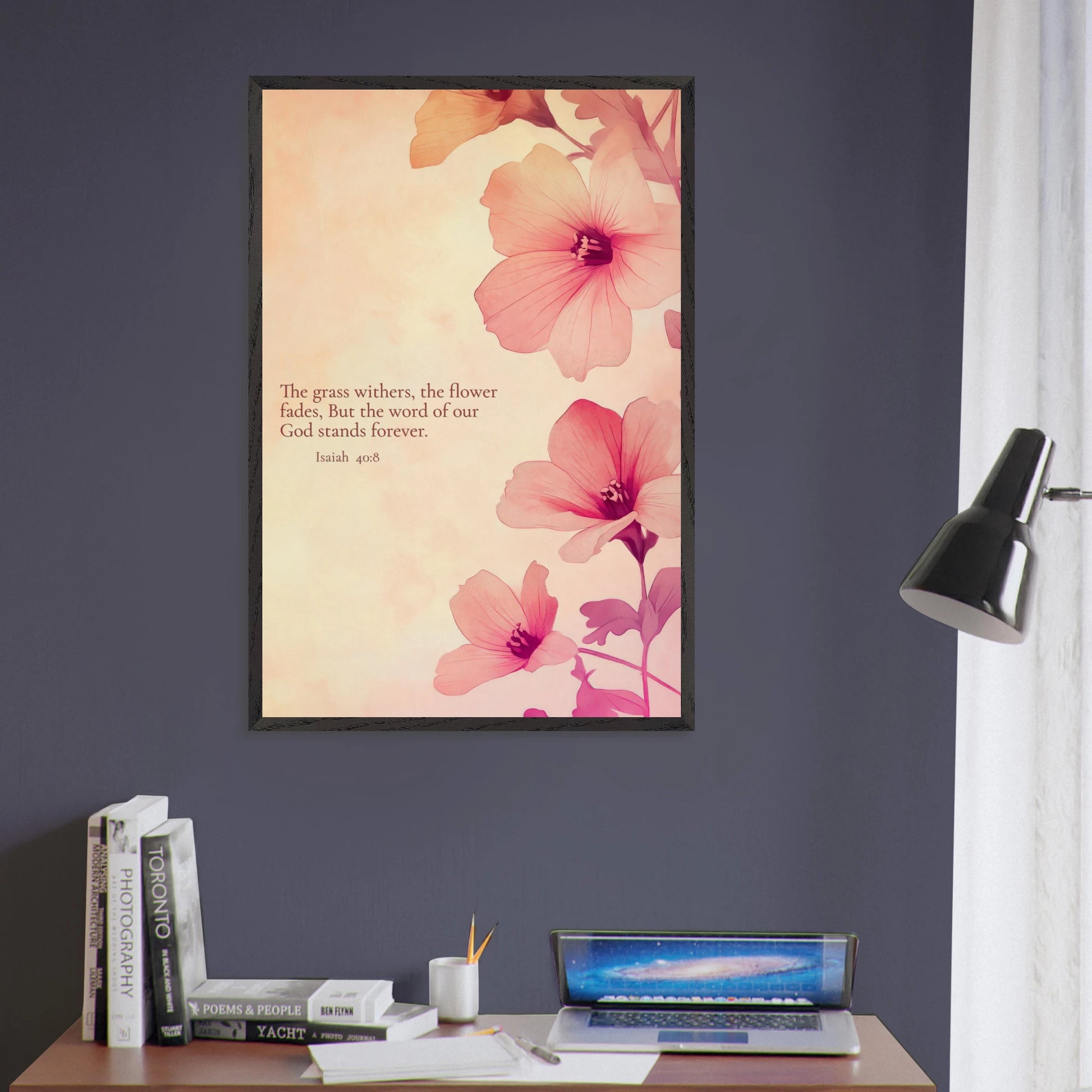 Framed Scripture art with soft pink flowers and Isaiah 40:8 hanging above a desk in a modern workspace with dark blue walls.