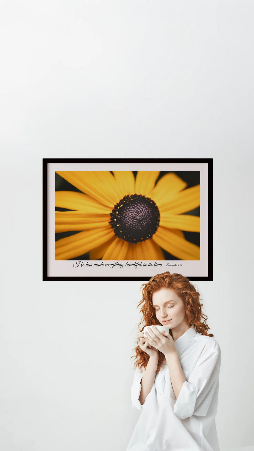 Woman holding a flower in front of a framed picture of a yellow flower on a white wall.
