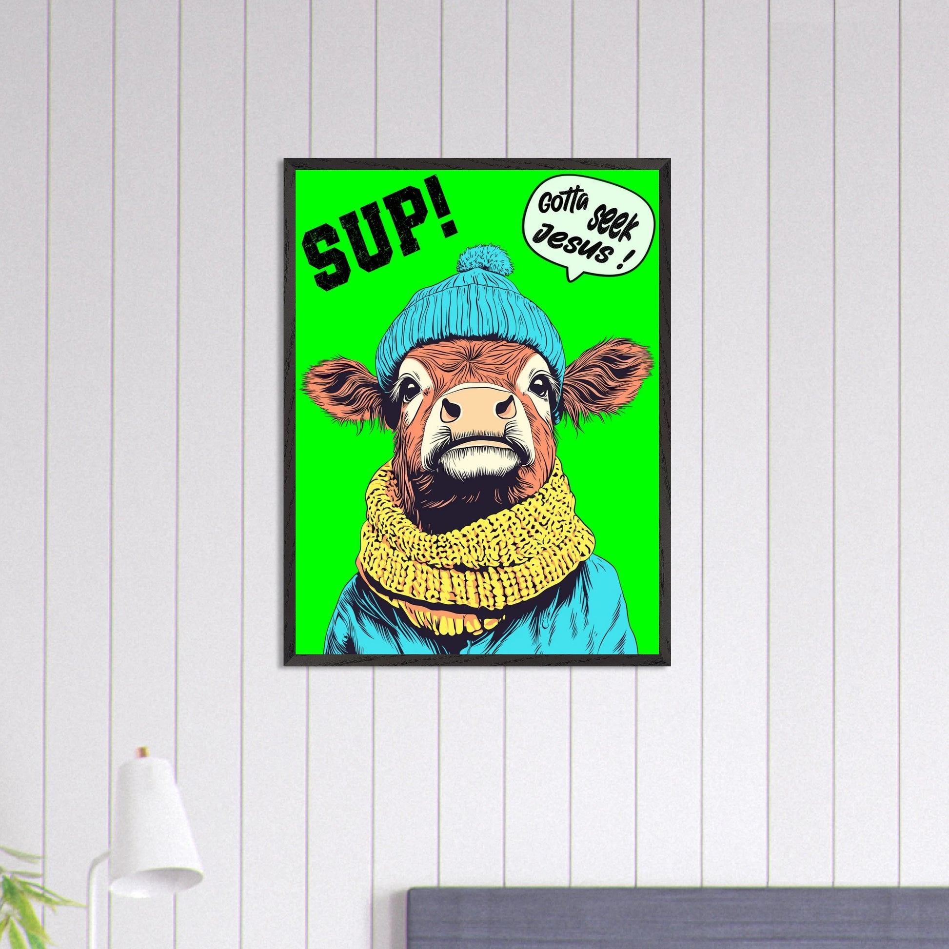 Playful Christian wall art featuring an illustrated cow wearing a blue beanie and yellow scarf on a bright green background, with SUP! and Gotta seek Jesus in a speech bubble, framed and hanging on a light wood-panel wall above a bed.