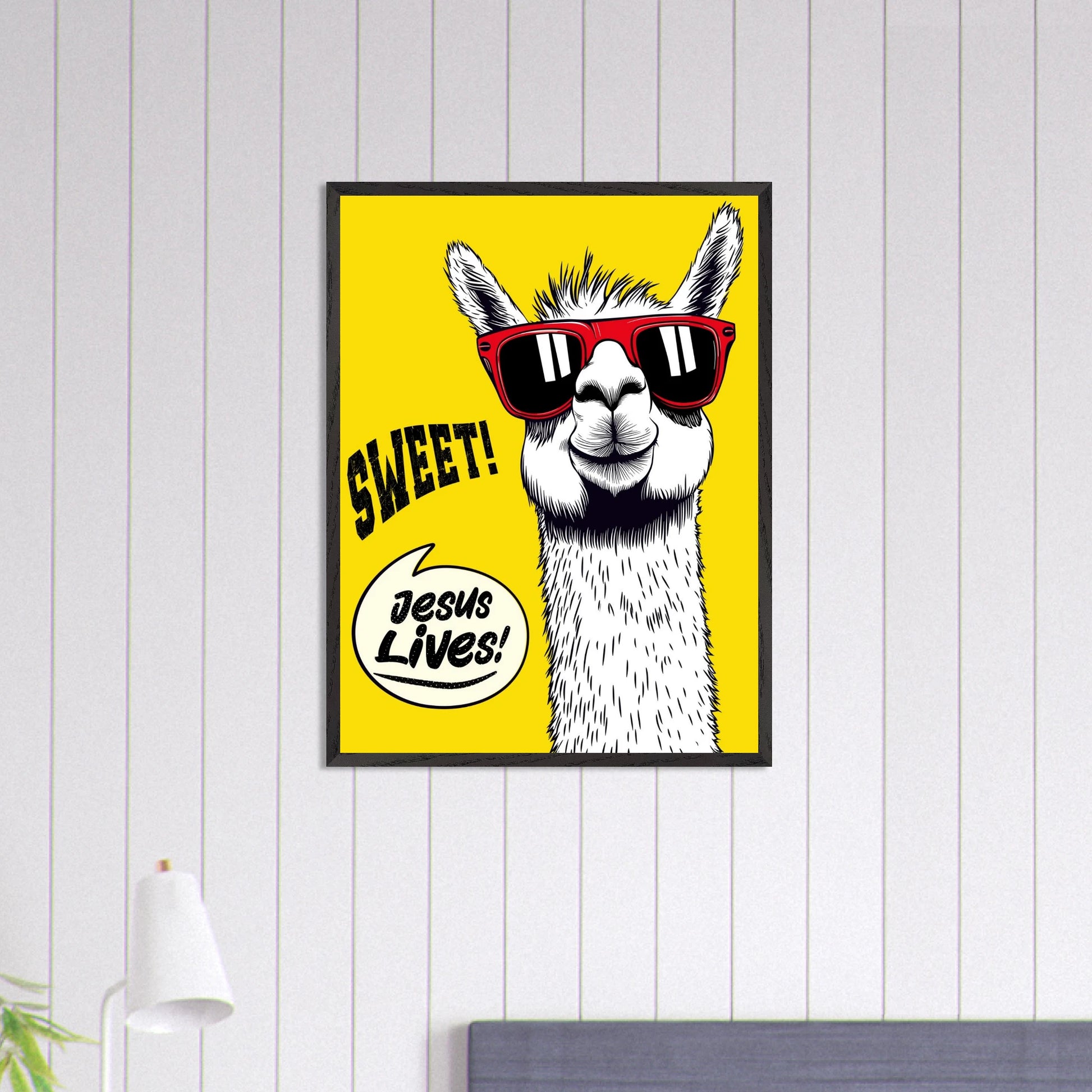 Framed Christian wall art featuring a white llama wearing red sunglasses on a bright yellow background with playful text reading SWEET and Jesus Lives, displayed in a modern bedroom setting