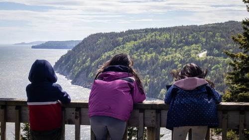 Three people in colorful jackets looking over a scenic view of a lake and forest.