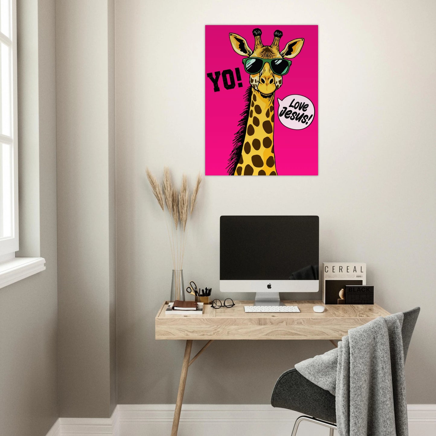 A colorful poster featuring a giraffe with sunglasses and a speech bubble that reads 'LOVE JESUS', set against a bold pink background displayed above a modern home office desk setup