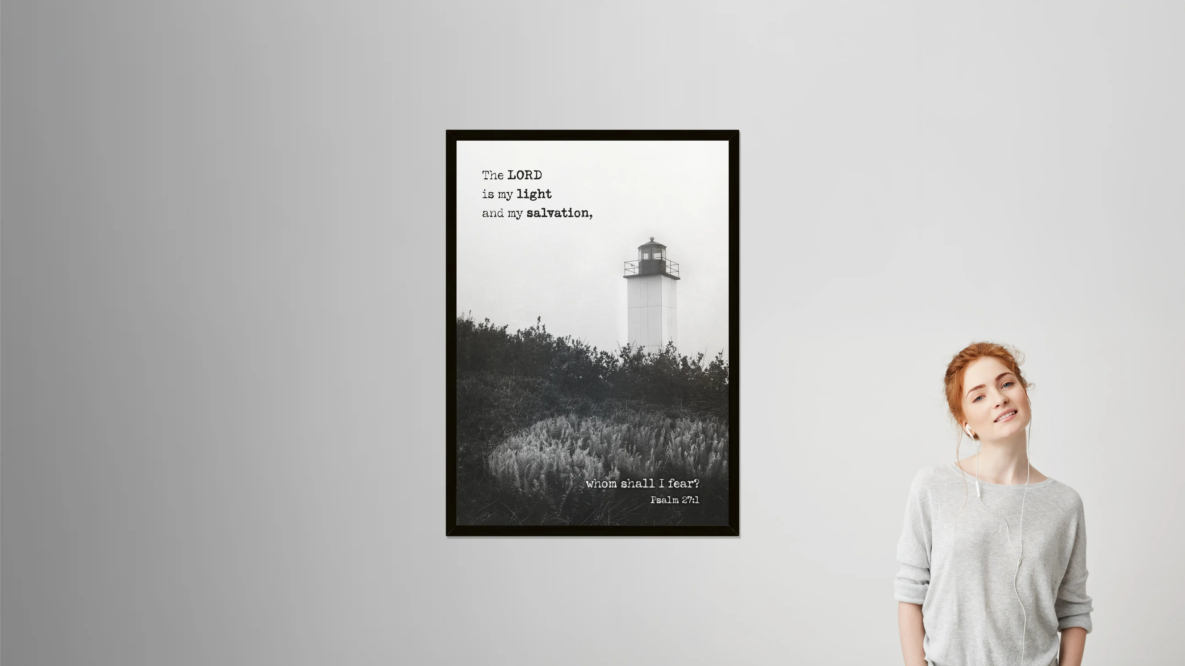 Framed black and white print of a lighthouse with text, displayed on a wall next to a person.