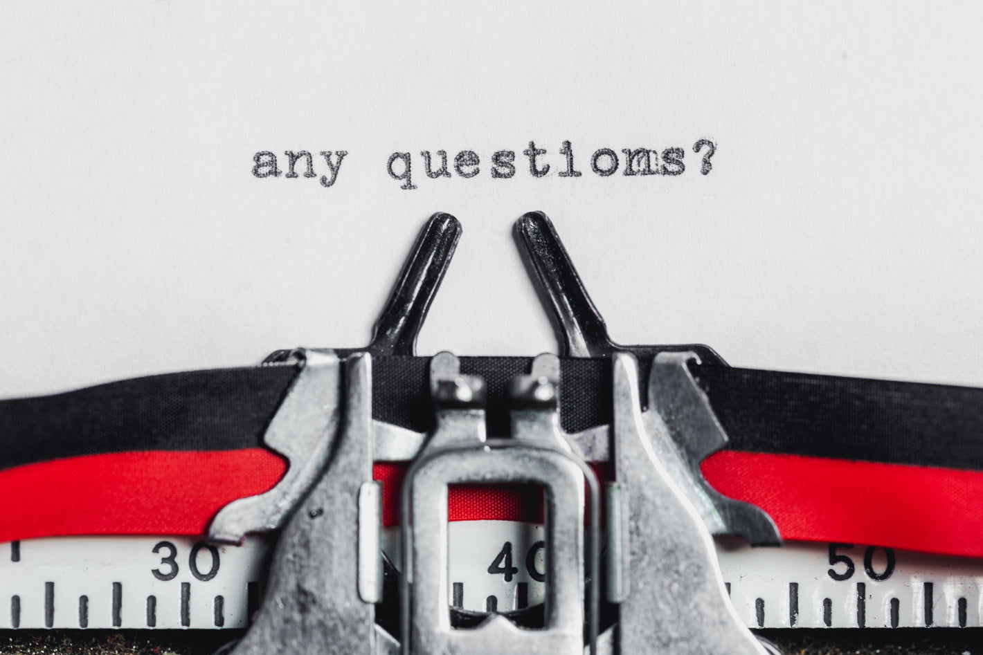A close-up of a typewriter typing the words “any questions?” on a sheet of paper.