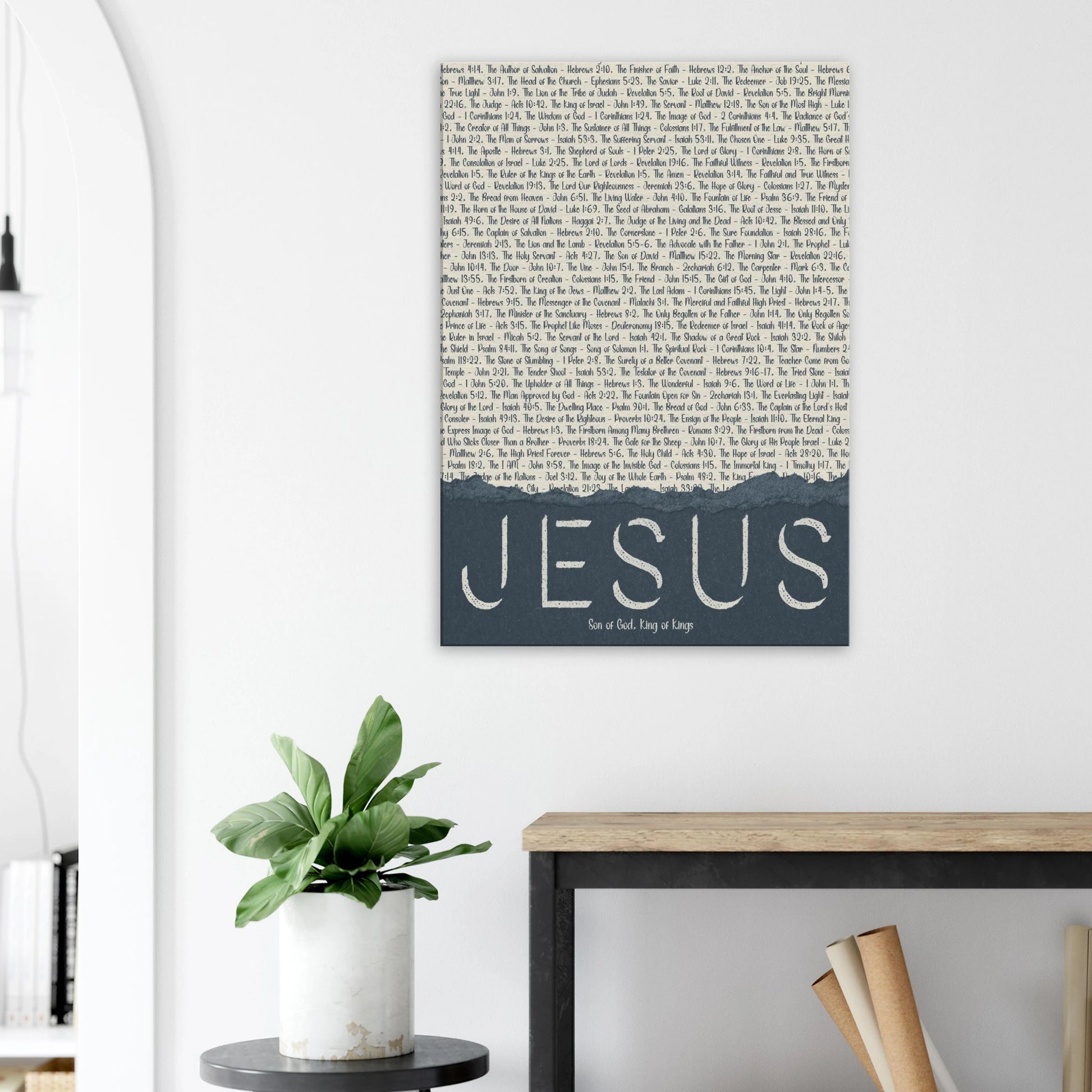 Wall art with 'Jesus' on a white wall above a desk and plant