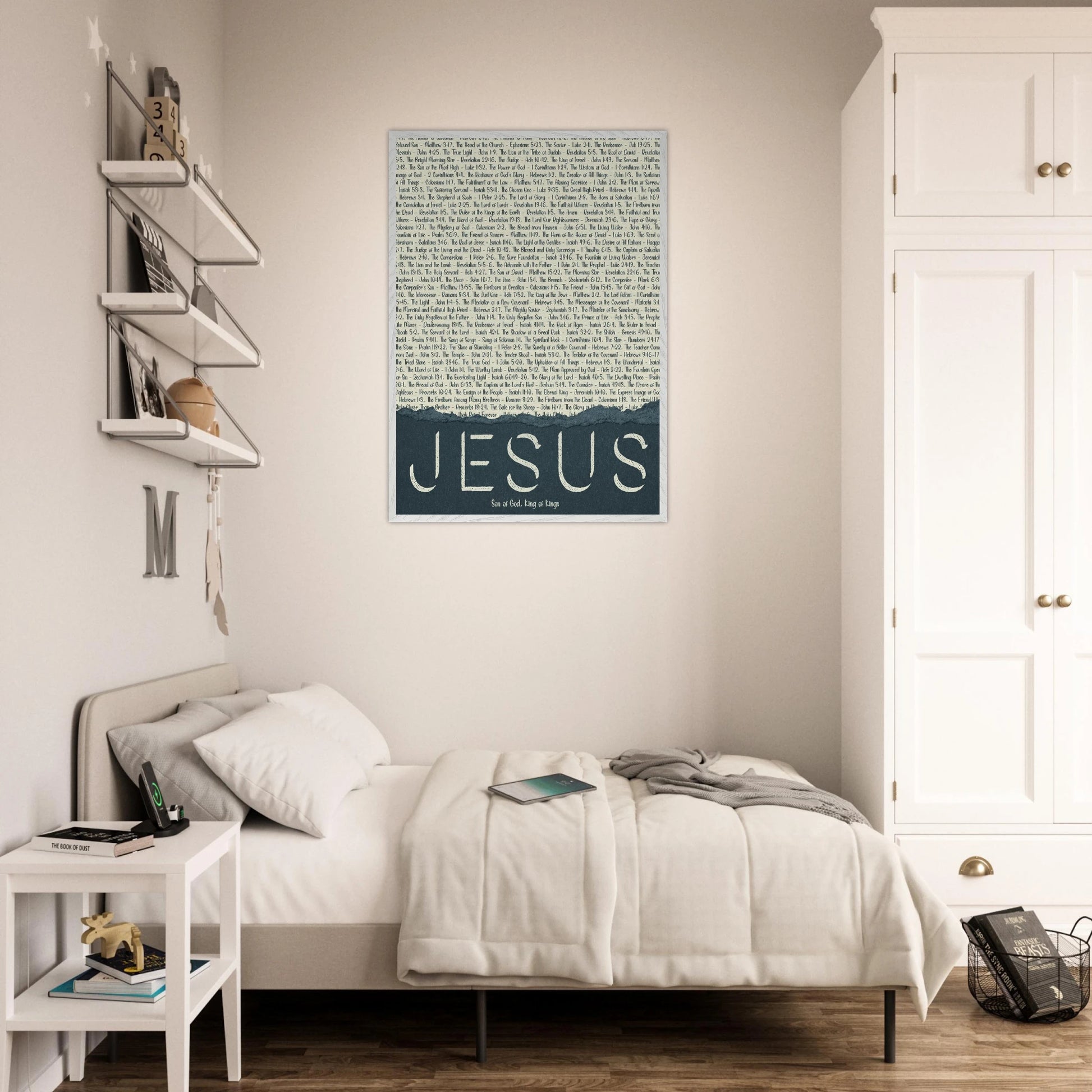 A framed wall art print with the word 'JESUS' in bold lettering, followed by a list of names and scriptures related to Jesus, against a white background hanging over a bright minimalist bedroom