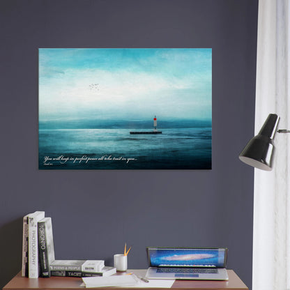 A wall art print featuring a lighthouse with a backdrop of the sea and sky, including a quote about perfect peace hanging over an office desk with lamp decor