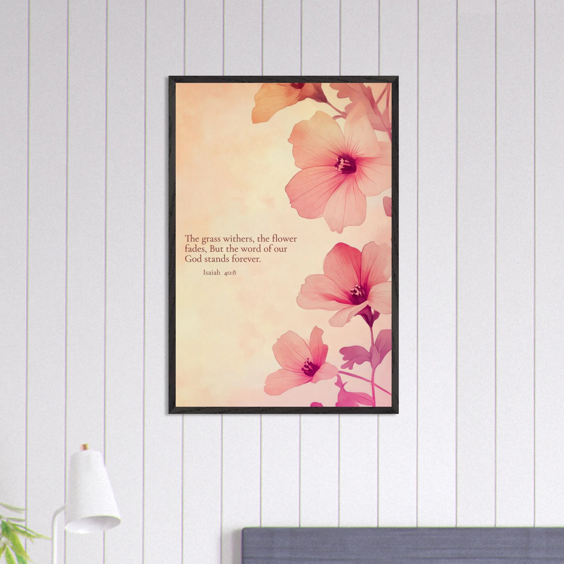 Pink floral framed Bible verse artwork with Isaiah 40:8 hanging on a light wood-panel wall above a bed.