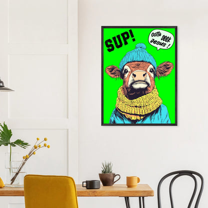 Playful Christian wall art featuring an illustrated cow wearing a blue beanie and yellow scarf on a bright green background, with SUP! and Gotta seek Jesus in a speech bubble, framed and hanging above a wooden table in a modern dining space