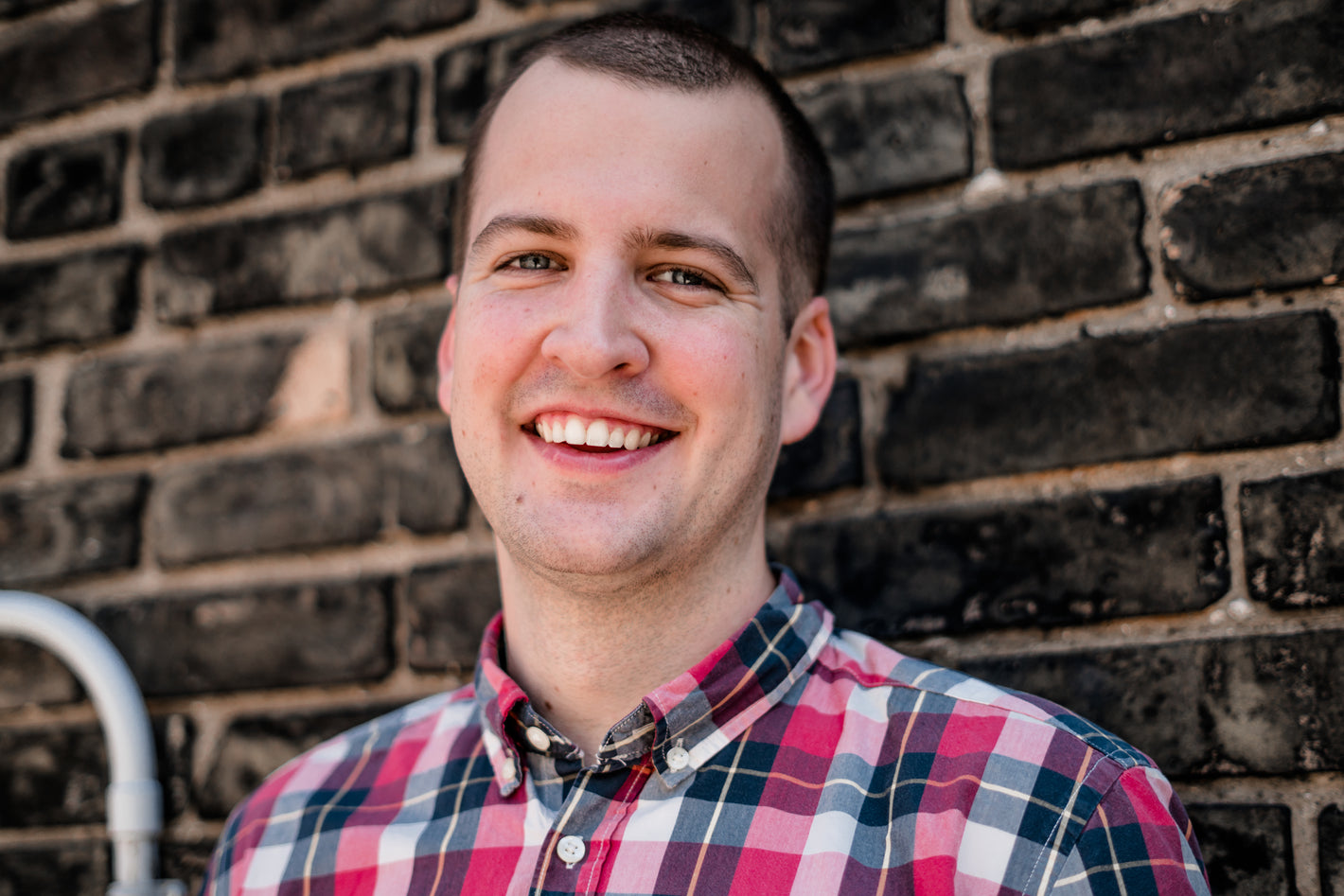 A person smiling while standing in front of a brick wall.