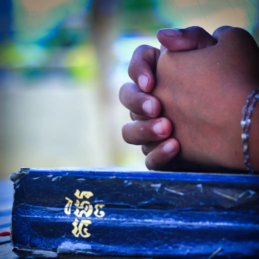 Praying hands on a blue Bible with a blurred background