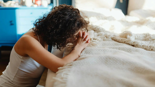 Person lying on a bed with a blanket, looking distressed.